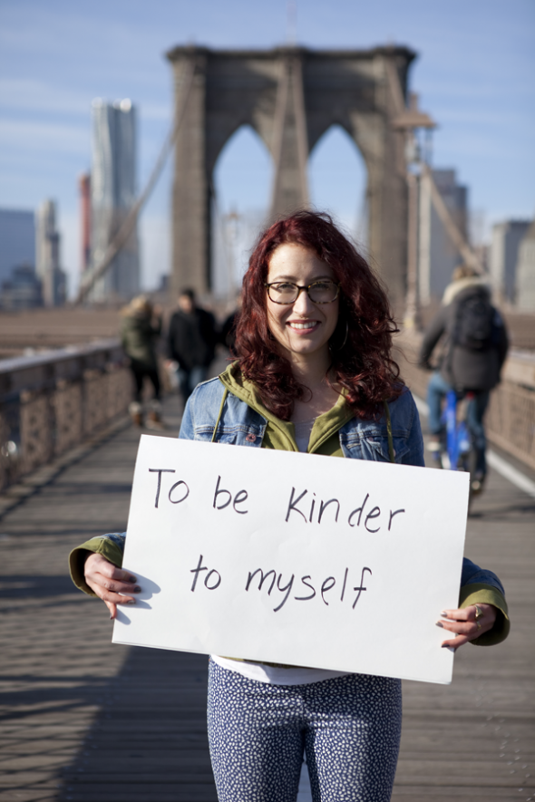 Photo of Sabina holding a sign that says "To Be Kinder To Myself"